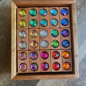 May include: A wooden tray with 24 iridescent gemstone blocks. The blocks are arranged in a grid pattern and are in various colors, including yellow, green, blue, purple, and red.