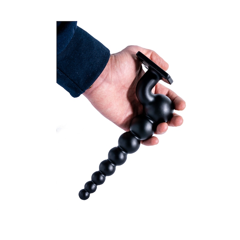 May include: A black rubber beaded toy with a flat base and a curved handle. The toy is made of multiple round beads connected together.