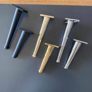 May include: Five furniture legs in different finishes: black, gold, and chrome. The legs are tapered and have a square base.