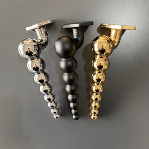 May include: Three decorative metal finials in gold, silver, and black. Each finial is a series of round balls connected together.