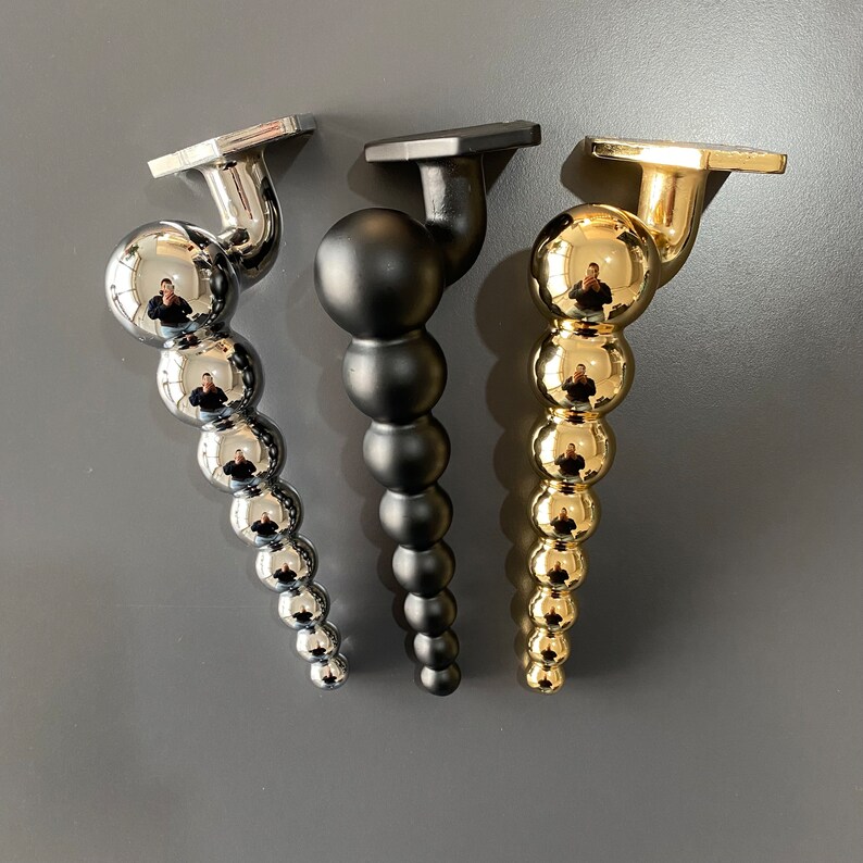 May include: Three decorative metal finials in gold, silver, and black. Each finial is a series of round balls connected together.