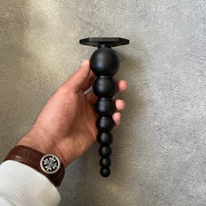 May include: A black metal phone stand with a series of round, black balls attached to the base. The stand is designed to hold a phone upright.