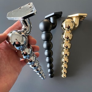 May include: Three decorative furniture legs with a ball and chain design. The legs are made of metal and are available in chrome, black, and gold finishes.