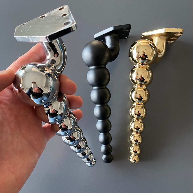 May include: Three decorative furniture legs with a ball and chain design. The legs are made of metal and are available in chrome, black, and gold finishes.