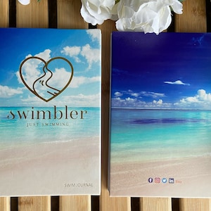May include: Two spiral-bound notebooks with beach and sky imagery. One notebook features the word "swimbler" with a heart-shaped design and the text "just swimming." The other notebook has a similar beach scene. The words "Swim Journal" are printed on the first notebook.