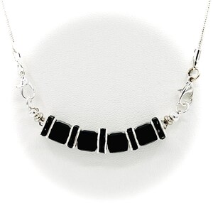 May include: A silver necklace featuring a series of rectangular black beads. The beads are connected by vertical silver bars and strung on a delicate silver chain. The necklace has a lobster clasp closure.
