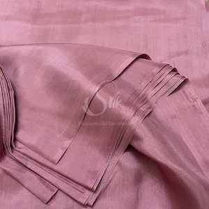 May include: A close-up of a folded piece of soft, pink silk fabric. The fabric has a subtle sheen and is smooth to the touch.