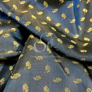 Könnte beinhalten: Nahaufnahme eines dunkelblauen Stoffes mit einem sich wiederholenden Muster aus goldfarbenen, stilisierten Blumen. Der Stoff hat einen dezenten Glanz und eine glatte Textur.