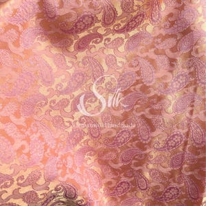 May include: A close-up of a pink and gold paisley patterned fabric. The fabric has a subtle sheen and a soft texture.