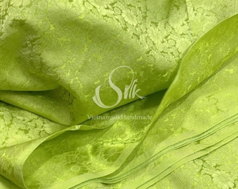 May include: A close-up of a bright green silk fabric with a floral pattern. The fabric is folded and draped, showing the texture and sheen of the silk. The text "VietnamsilkHandmade" is visible in the lower center of the image.