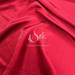 Puede incluir: Tela de seda roja con un patrón de rosas. La tela es lisa y tiene un brillo sutil. El texto "VietnamsilkHandmade" es visible en el centro inferior de la imagen.