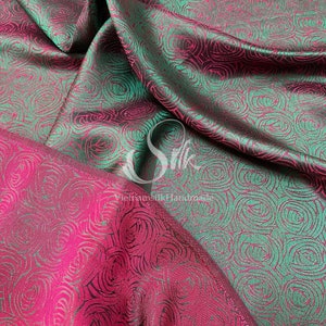 May include: A close-up of a fabric with a repeating pattern of pink and green roses. The fabric is smooth and silky.
