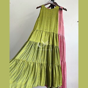 May include: A green sleeveless maxi dress with a tiered skirt and a pink sleeveless maxi dress with a tiered skirt. Both dresses are hanging on a wooden hanger.