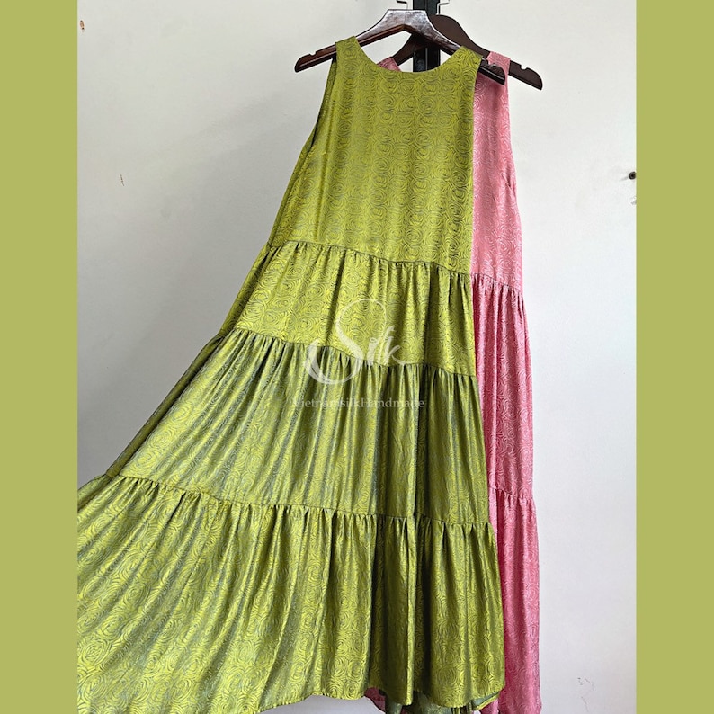 May include: A green sleeveless maxi dress with a tiered skirt and a pink sleeveless maxi dress with a tiered skirt. Both dresses are hanging on a wooden hanger.