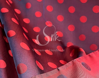 May include: Red silk fabric with a polka dot pattern. The dots are a darker shade of red and are raised. The fabric is folded over and the underside is a darker shade of red with black polka dots.