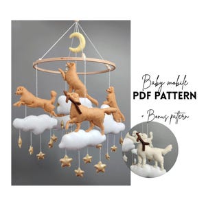 Könnte beinhalten: Baby-Mobile mit Filz-Golden Retriever-Hunden, weißen Wolken, goldenen Sternen und einem Mond. Das Mobile hängt an einem Holzreifen. Der Text "Baby mobile PDF pattern + Bonus pattern" ist sichtbar.