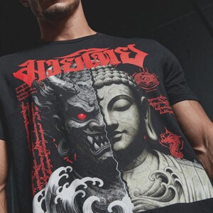 May include: A black short-sleeved t-shirt featuring a split-face graphic of a demonic figure with a glowing red eye and a serene Buddha. The design includes red Thai script at the top, red text accents, a red dragon illustration, and white wave patterns.