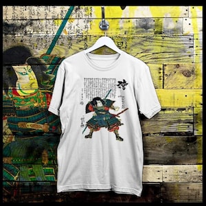 May include: White t-shirt with a black and white illustration of a samurai warrior holding a sword. The illustration is surrounded by Japanese text.
