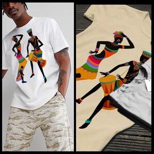 May include: White t-shirt with a colorful graphic print of three silhouettes of people dancing. The people are wearing traditional African clothing and holding drums.