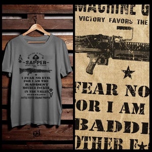 May include: A gray t-shirt with a black graphic design featuring a machine gun, spades, and the text "I fear no evil for I am the baddest mother facher in the valley. Battle tested combat proven."