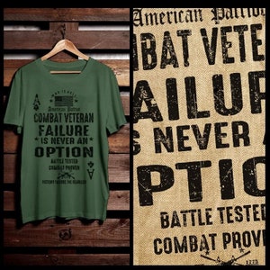 Puede incluir: Una camiseta verde con una impresión negra que dice "War is Hell. American Patriot. Combat Veteran. Failure is never an option. Battle Tested. Combat Proven. Victory Favors the Fearless." La camiseta está colgada de una percha de madera sobre un fondo de panel de madera.