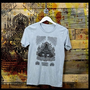 May include: A light gray t-shirt with a black and white graphic print of a deity in a seated position. The graphic is surrounded by intricate patterns and text in a foreign language.