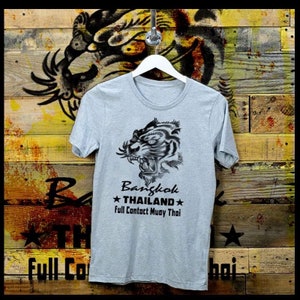May include: A gray t-shirt with a black and white illustration of a tiger's head. The text "Bangkok *THAILAND* Full Contact Muay Thai" is printed on the shirt.