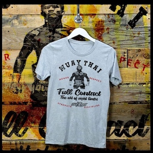 May include: A gray t-shirt with a vintage-style graphic design featuring the words "Muay Thai" and "Full Contact" in black text. The graphic also includes a silhouette of a Muay Thai fighter in a fighting stance. The words "Honor", "Respect", "Strength", and "Discipline" are printed in red text around the graphic.