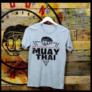 May include: A gray t-shirt with a black and white graphic print of a fist in a triangle with the text "The Science of Eight Limbs Muay Thai".
