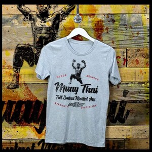 May include: A gray t-shirt with a black graphic of a Muay Thai fighter with the text "Muay Thai Full Contact Martial Arts" and the words "Honor, Respect, Strength, Discipline" around the graphic.