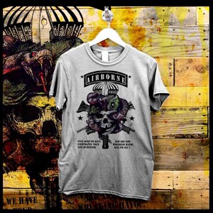 May include: A light gray t-shirt with a graphic design featuring a skull, snakes, and guns. The word "AIRBORNE" is printed across the top. The shirt also has text that reads "ONCE AGAIN WE HAVE INFILTRATED YOUR LINE OF DEFENSE" and "AND ARE NOW WREAKING HAVOC. KILL EM ALL!!"