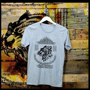 May include: A grey t-shirt with a black and white illustration of a tiger's head with a temple in the background. The design includes Thai script.