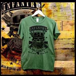 Puede incluir: Camiseta verde con una calavera que lleva un casco militar y un pañuelo. La calavera sostiene dos rifles cruzados delante de ella. El texto "INFANTRY" está por encima de la calavera y "BORN TO RAISE HELL" está por debajo de la calavera. El texto "MESS WITH THE BEST DIE LIKE THE BEST" está por debajo de la calavera.
