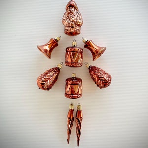 May include: A collection of vintage Christmas ornaments in shades of copper and bronze. The ornaments include a Santa Claus figure, bells, drums, pinecones, and icicle-shaped decorations. Each ornament has a metallic finish and a loop for hanging.