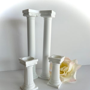 May include: Set of four white plastic columns, varying in height, with fluted detailing. The columns are perfect for cake decorating or other craft projects.