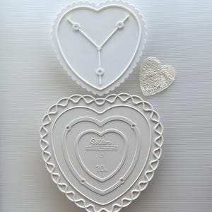 May include: White heart-shaped cake decorating stencils and a small lace heart. The stencils have scalloped edges and include the text "Wilton Decorator Preferred" and the number "10".
