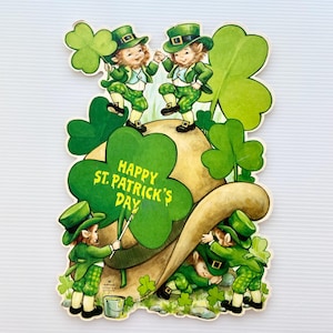 May include: Vintage St. Patrick's Day greeting card featuring leprechauns in green outfits and hats. The card has a large shamrock and the text "Happy St. Patrick's Day". The illustration has a whimsical, cartoon style.