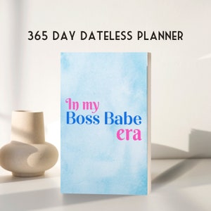 May include: A blue and white watercolor planner with the text "In my Boss Babe era" in pink and blue lettering. The planner is a 365 day dateless planner.