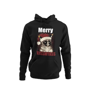 Op de afbeelding: Zwarte hoodie met een witte afbeelding van een chagrijnige kat die een kerstmanmuts draagt. De tekst "Merry Kiss My Ass" staat onder de kat.