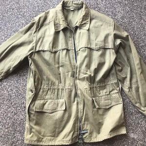 Könnte beinhalten: Eine grüne Utility-Jacke mit Reißverschluss, zwei großen Taschen und einem Kordelzug an der Taille.