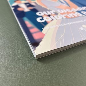 Może przedstawiać: Biała i niebieska książka do kolorowania ślubnego z tekstem "Our Wedding Coloring Book" i "Color Your Memories" na okładce.