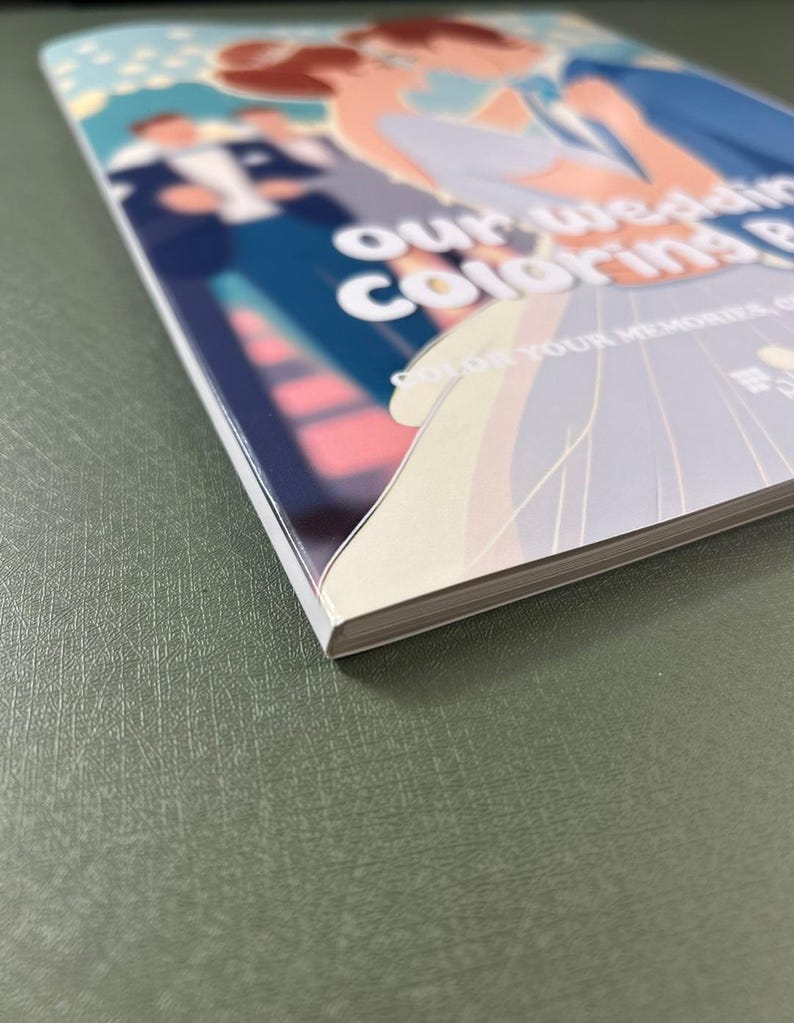 Może przedstawiać: Biała i niebieska książka do kolorowania ślubnego z tekstem "Our Wedding Coloring Book" i "Color Your Memories" na okładce.