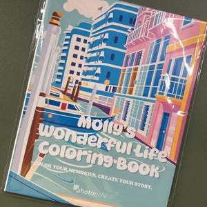 Może przedstawiać: Kolorowa książka do kolorowania z tytułem "Molly's Wonderful Life Coloring Book" i hasłem "Koloruj swoje wspomnienia, stw&oacute;rz swoją historię." Okładka przedstawia ilustrację kanału z budynkami po obu stronach i łodzią w wodzie.