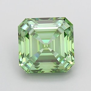 Puede incluir: Una piedra preciosa de corte cuadrado con un tono verde claro, que presenta un patrón de facetas en escalera que crea una serie de reflejos rectangulares concéntricos. La piedra muestra un alto grado de claridad y brillo con bordes geométricos nítidos.