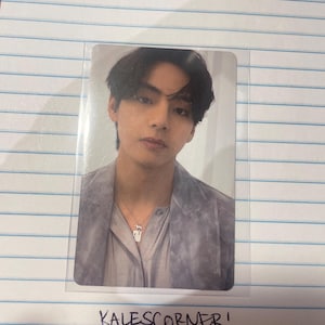 Puede incluir: Fotografía de una persona con una chaqueta gris y un collar plateado. La foto está en una funda de plástico transparente. El texto "KALESCORNER!" está escrito con tinta negra debajo de la foto en papel rayado.
