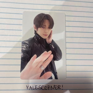 May include: A photo card featuring a person wearing a black leather jacket and a silver ring. The person is touching their face with one hand and extending the other hand towards the camera. The text "KALESCORNER!" is at the bottom.