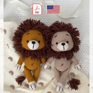 Può includere: Due leoni di peluche all'uncinetto fatti a mano. Uno è giallo dorato, l'altro rosa chiaro. Entrambi hanno criniere marroni, musetti bianchi e dettagli bianchi sulle zampe. I leoni sono alti circa 20 cm.