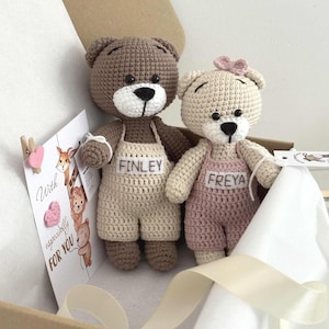 Könnte beinhalten: Zwei gehäkelte Teddybären, einer braun und einer beige, tragen Latzhosen mit den Namen "FINLEY" und "FREYA". Eine Karte mit dem Text "With especially FOR YOU" ist an der Box befestigt. Der beige Bär hat eine rosa Schleife.