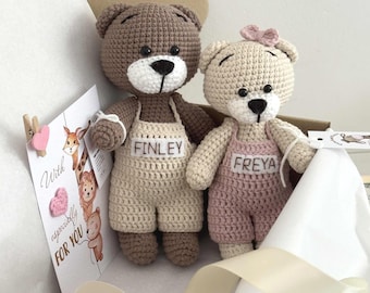 May include: Two handmade crochet teddy bears, one brown and one beige, wearing overalls with names "FINLEY" and "FREYA". A card with the text "With especially FOR YOU" is clipped to the box. A pink bow adorns the beige bear.