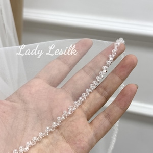 May include: A white bridal veil with a beaded edge. The veil is held in a hand, and the text "Lady Lesilk" is visible in the upper left corner.